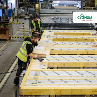 Workers in high-visibility vests assembling insulated timber wall panels inside a modern offsite construction factory.
