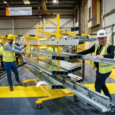 Workers in safety vests and hard hats operating mechanical lift equipment in a warehouse.