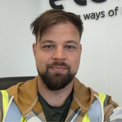 A person wearing a high-visibility vest and brown jacket against a light background.