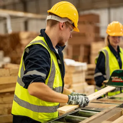 Construction workers in yellow hard hats and safety vests working with wooden materials in a workshop.