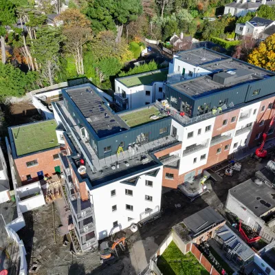 Aerial view of a multi-storey residential building under construction surrounded by trees and nearby houses.