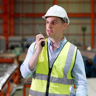 Worker in hard hat and safety vest standing in an industrial warehouse environment.