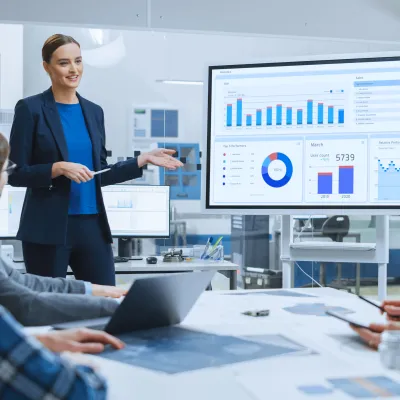 Person in blue jacket presenting data charts to colleagues in modern office meeting room.