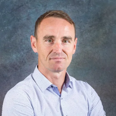Professional portrait photograph of person in light blue shirt against a dark blue background.