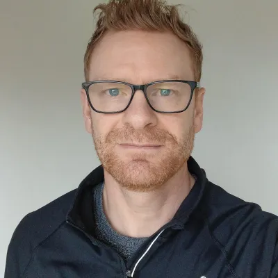 Person with short light hair and glasses wearing a black top with the Cygnum logo, standing against a plain background.