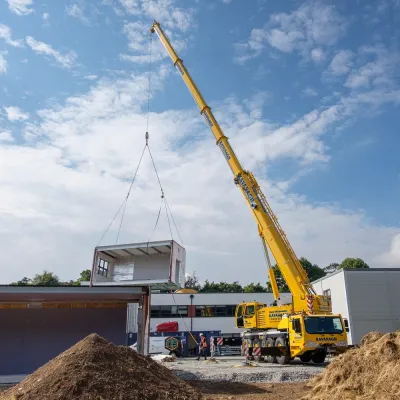 Yellow crane lifting construction materials at building site under blue sky.