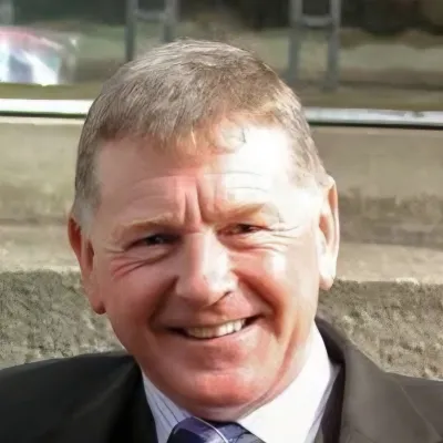 A person in a suit and tie smiling outdoors with stone steps visible in the background.