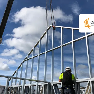 Construction worker in safety gear inspecting steel frame building structure against blue sky