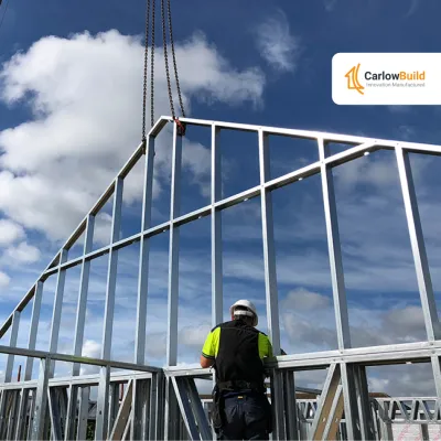 Construction worker installing metal frame structure against blue sky with clouds.