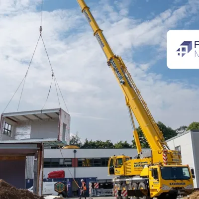 Yellow crane lifting a large modular structure at a construction site under blue sky.