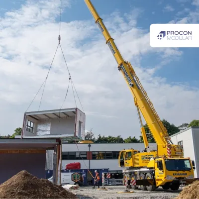 Yellow crane lifting a modular building structure at a construction site under blue sky.