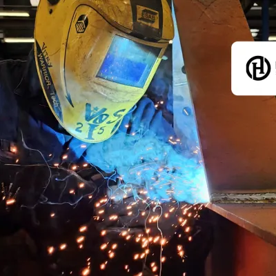 Welder in protective helmet working with bright blue sparks in industrial setting.