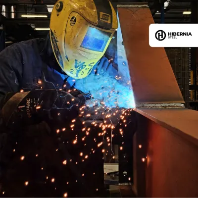 Welder in protective gear with bright sparks flying during metalwork fabrication.