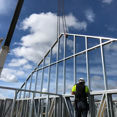 Construction worker in safety gear assembling metal framework against blue sky with clouds.