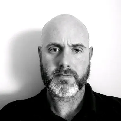 Black and white portrait of a bald person with beard wearing black against white background.