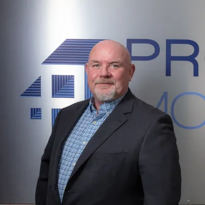 Professional man in business attire standing in front of a corporate logo with blue and gold text.