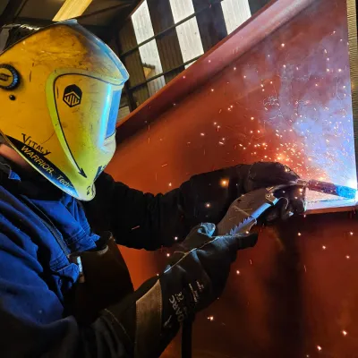 Welder in protective helmet creating bright orange sparks on metal surface.