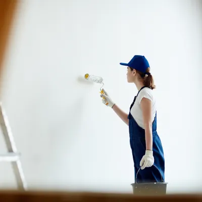 Person in blue cap and tank top painting a wall with a roller