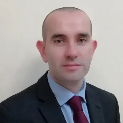 Professional portrait of a person in dark suit with red tie against light background.