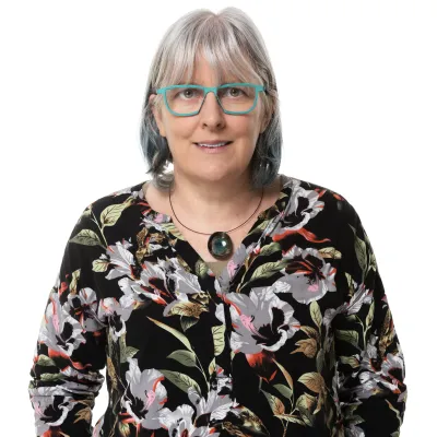 Woman with glasses and gray hair wearing a black floral patterned blouse.