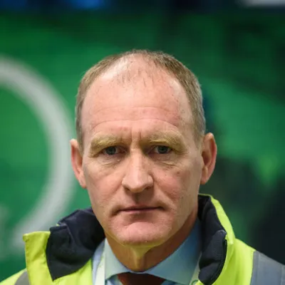 A person wearing a high-visibility safety vest and red tie against a green background.