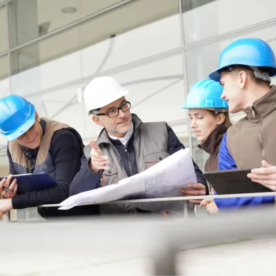 Construction professionals in blue hard hats examining blueprints at a worksite.