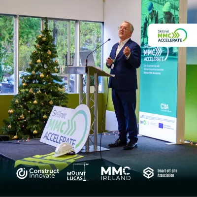 Person in suit speaking at a podium next to a Christmas tree and event banners.