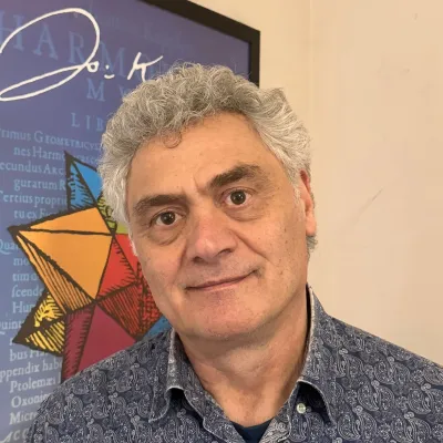 A person with gray hair wearing a dark shirt standing in front of a wall display with a colorful geometric design.
