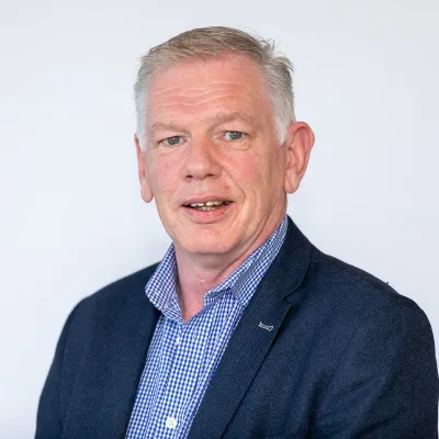 Professional headshot of a person with gray hair wearing a navy blazer and patterned blue shirt