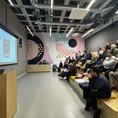 A lecture hall with tiered seating where attendees watch a presentation on a large screen.