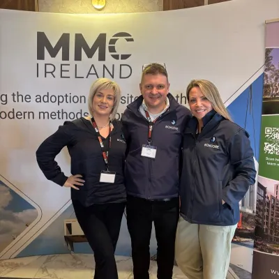 Three people posing together at an MMC Ireland conference display booth.