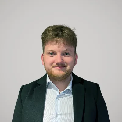 Professional headshot of person in dark suit with light blue shirt against white background.