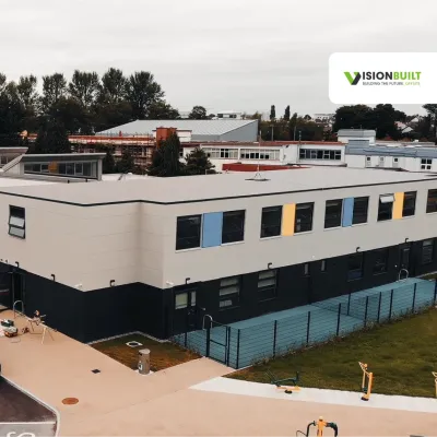 Modern educational facility with colorful accents, surrounded by trees and parking area.