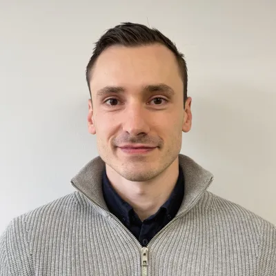 Person wearing a gray turtleneck sweater against a beige background.