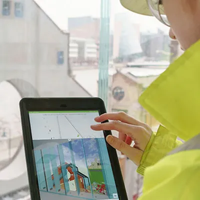 Person in bright yellow safety jacket using a tablet at a construction site window.
