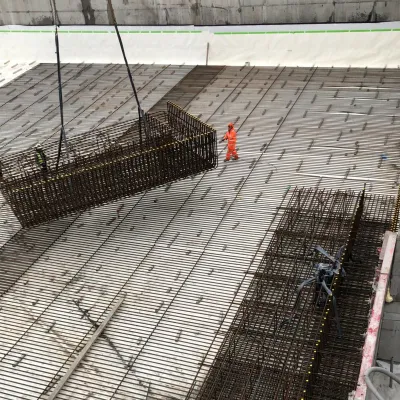 Construction site with steel reinforcement bars laid on concrete, being lifted by cables.