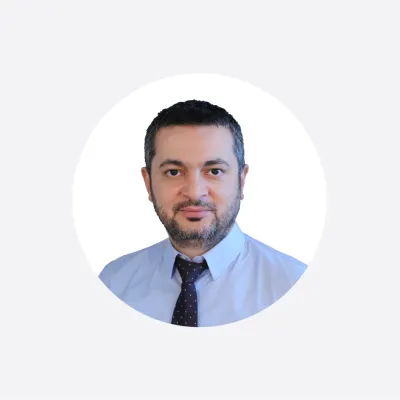 Professional headshot of a man with a beard wearing a light blue shirt and dark tie.
