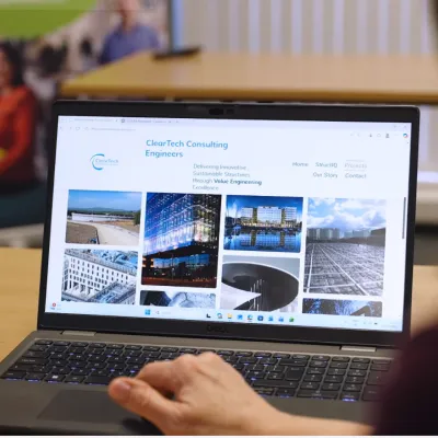 Hands typing on a laptop displaying a consulting firm's website with building images.