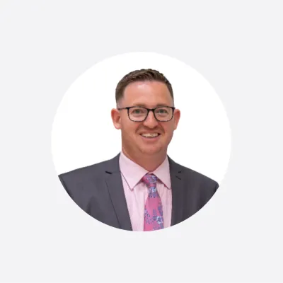 Professional headshot of a smiling man in a gray suit and pink floral tie wearing glasses.