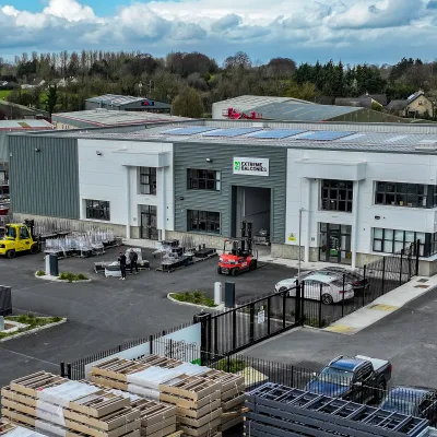 Aerial view of an industrial warehouse complex with solar panels, vehicles, and stacked materials outside.