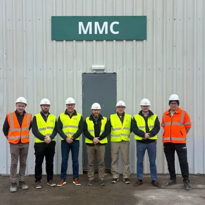 Seven people in hard hats and high-visibility vests standing outside an MMC building.