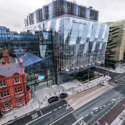 Aerial view of a modern glass building beside a historic red-brick structure on a city street.