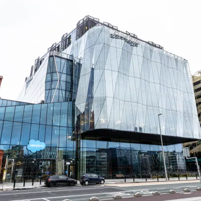 Modern glass and steel building with angular facade on an urban street corner, overcast sky.