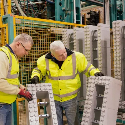 Two workers in yellow safety vests inspecting metal components on a factory floor.