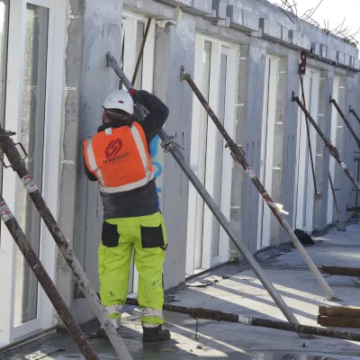 Construction worker in orange safety vest and yellow pants working on a building site.