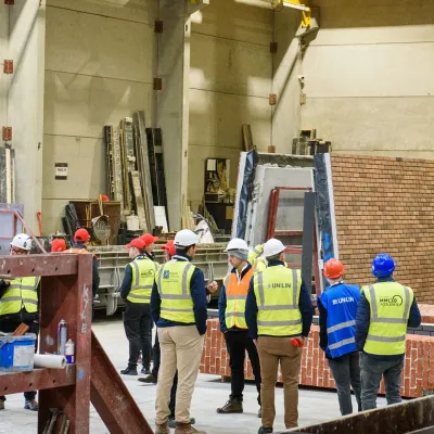 Group of workers in yellow safety vests observing construction work inside a large industrial building.