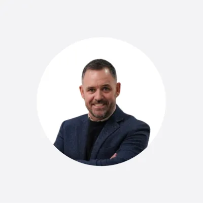 Professional headshot of a smiling man in a navy blazer with arms crossed.