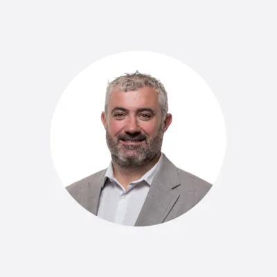 Professional headshot of a smiling middle-aged man with a beard, wearing a gray blazer.