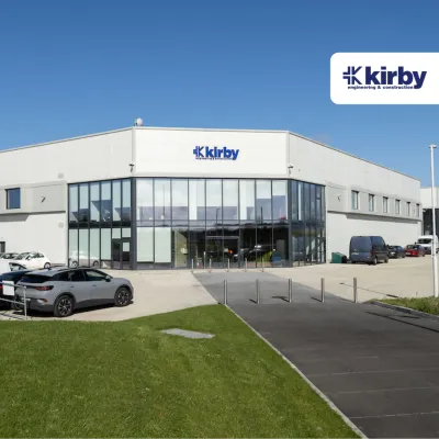Modern Kirby building exterior with parked cars, glass facade, and blue sky.