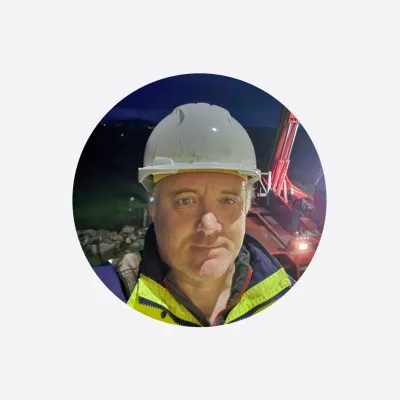 Man in white hard hat and high-visibility vest at a construction site at night.